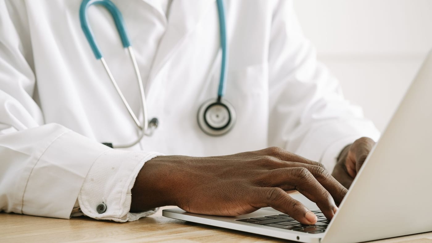 Médico digitando em um notebook em um consultório organizado